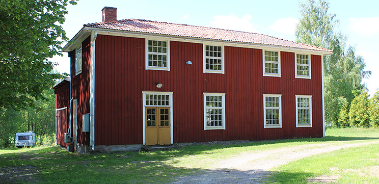 En röd stor byggnad i trä med stora fönster, med flera små fönsterrutor i varje fönster. 