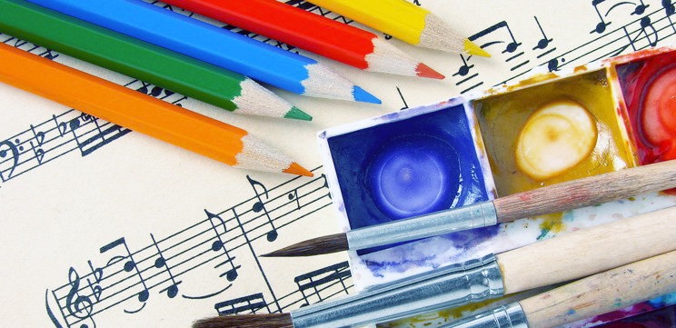 Färgpennor, penslar och akvarelfärger ligger utlagda på ett notblad. 