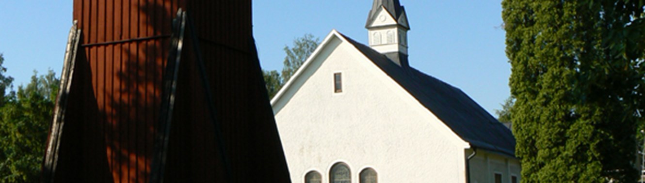 En vit kyrka med en klockstapel av trä i förgrunden. 