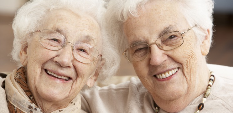 Två äldre kvinnor tittar in i kameran och ler. 